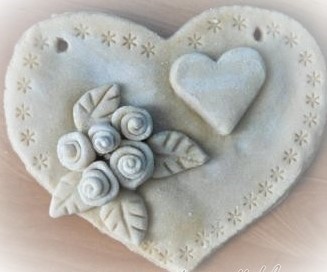 Serce z masy solnej w kolorze białym przyozdobione mniejszym białym sercem w środku oraz pięcioma różyzckami i czteroma listakmi.