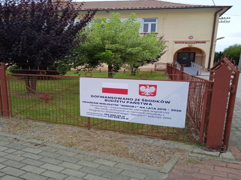 Zdjęcie przedstawia tablicę informacyjną dofinansowania zadania remontu pomieszczeń na parterze budynku szoły podstawowej w Jadownikach Mokrych na potrzeby Klubu Seniora.