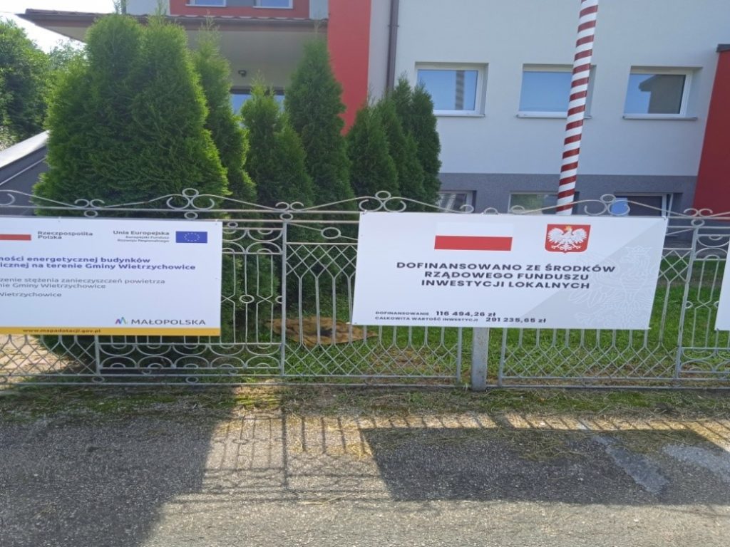 Zdjęcie przedstawia tablicę informacyjną o dofinansowaniu zadania poprawy efektywności energetycznej budynku OSP w Jadownikach Mokrych.
