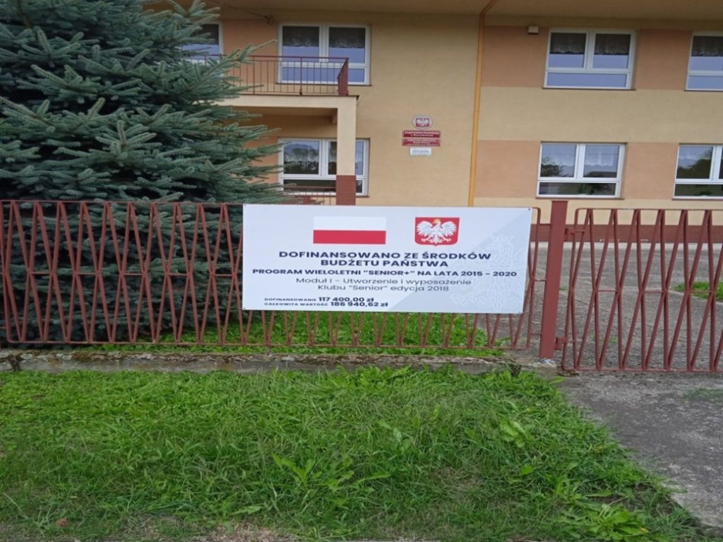Zdjęcie przedstawia tablicę informacyjną zadania remonmt pomieszceń w budynku Gimnazjum w Miechowicach Wielkich na potrzeby Klubu Seniora.